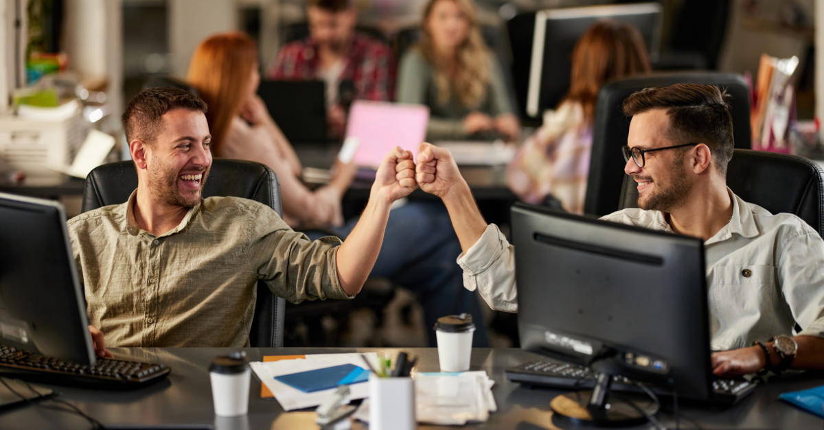 Two males fist bumping success in an office environment.png